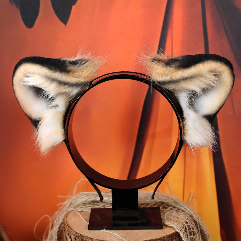 Puede incluir: Una diadema negra con dos orejas de animal de piel sint&eacute;tica. Las orejas tienen un patr&oacute;n de color degradado con puntas negras, secciones centrales de color tostado y detalles de pelo blanco en la parte interna de la oreja.