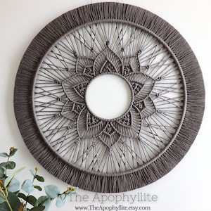 May include: A large grey macrame wall hanging with a circular shape and a detailed mandala design. The hanging has a fringe border.