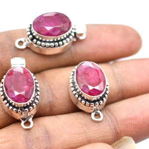 May include: Three silver oval-shaped clasps with red ruby gemstones. Each clasp has a decorative beaded border and a loop on the bottom.