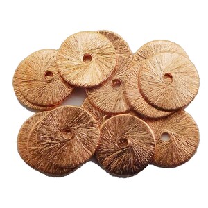 Peut inclure: Un tas de 10 embellissements ronds en métal de couleur cuivre avec un trou au centre. Les embellissements ont un design texturé en forme de soleil.