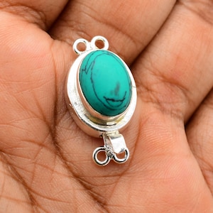 Puede incluir: Cierre de tono plateado con una piedra ovalada turquesa. El cierre tiene dos bucles a cada lado para sujetar las joyas.