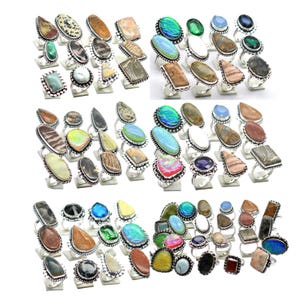 May include: A selection of gemstone rings featuring diverse shapes and colours, such as oval, teardrop, and rectangular stones. The rings have silver-coloured bands and display a variety of natural stone patterns and hues.