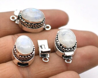 Op de afbeelding: Een verzameling zilverkleurige sieradssluitingen met ovale, iriserende maansteen cabochons. De sluitingen hebben decoratieve, golvende patronen en zijn ontworpen voor het maken van sieraden. De afbeelding toont de sluitingen in verschillende stadia van montage.