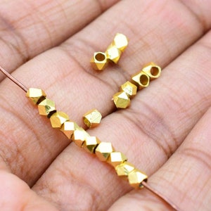 May include: Gold-toned metal beads with a faceted design. The beads are strung on a thin wire and are approximately 4mm in diameter.
