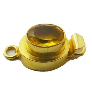 Puede incluir: Cierre dorado con una piedra preciosa redonda de forma ovalada, de color amarillo.
