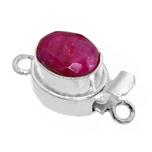 Pode incluir: Fecho prateado com uma gema oval vermelha. O fecho tem dois laços para prender a um colar ou pulseira.