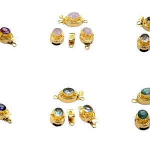 May include: A collection of gold-colored jewelry clasps, each featuring a different colored gemstone. The gemstones include pink, purple, clear, blue, and green. The clasps are oval-shaped with a small loop on each end.