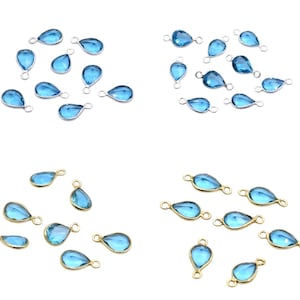 Puede incluir: Cuatro conjuntos de colgantes de cristal azul en forma de lágrima. Dos conjuntos tienen bordes y bucles de metal plateado, mientras que los otros dos tienen bordes y bucles de metal dorado. Los colgantes están dispuestos sobre un fondo blanco.