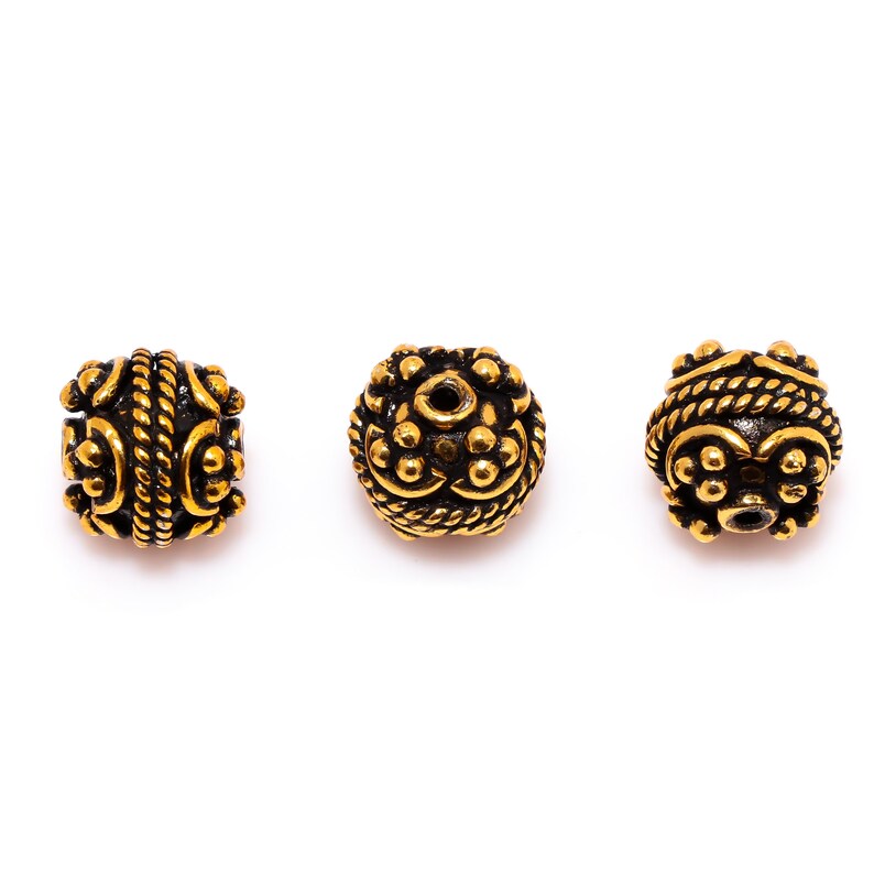 May include: Three gold-toned metal beads with intricate designs. The beads have a black finish and are round with a hole in the center.