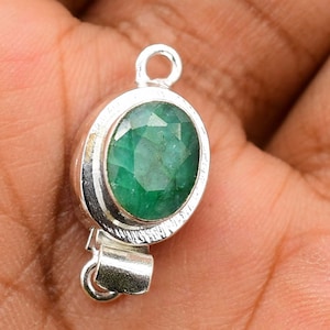 May include: A silver clasp with a green oval emerald gemstone. The clasp is designed to be used for necklaces or bracelets.