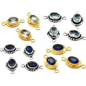 May include: A collection of oval gemstone connectors in gold and silver settings. The gemstones are either light blue or dark blue. Each connector has two loops for attaching to other components.