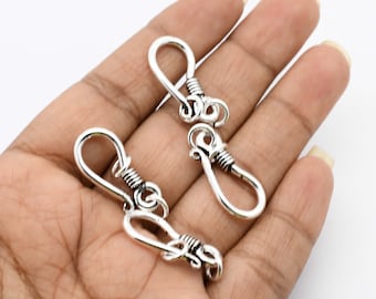 May include: Two silver-toned metal clasps with a decorative design. The clasps are open and ready to be attached to a necklace or bracelet.