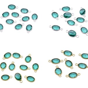 Könnte beinhalten: Eine Auswahl an ovalförmigen, teal-farbenen Edelsteinanhängern. Einige Anhänger haben silberfarbene Metalleinfassungen, andere goldfarbene. Die Anhänger werden vor einem weißen Hintergrund präsentiert.