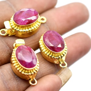 Könnte beinhalten: Drei goldfarbene ovale Verschlüsse mit roten Edelstein-Akzenten. Jeder Verschluss hat einen dekorativen Perlenrand.