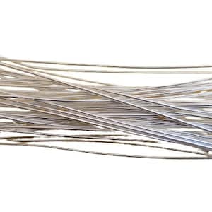 May include: A pile of silver-colored head pins, each with a small ball at one end. The pins are straight and appear to be made of metal. They are scattered against a white background, suggesting a craft or jewelry-making theme.