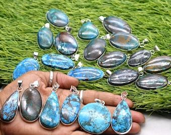 Op de afbeelding: Een verzameling ovale en druppelvormige hangers met gepolijste blauwe en bruine stenen in zilverkleurige metalen monturen. De hangers vertonen gevarieerde patronen van turquoise, blauwgroene en donkerbruine aders op hun gladde oppervlakken.