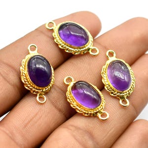 Op de afbeelding: Vier ovale hangers in goudkleur met amethist edelstenen. Elke hanger heeft twee springringen om aan een ketting of armband te bevestigen.