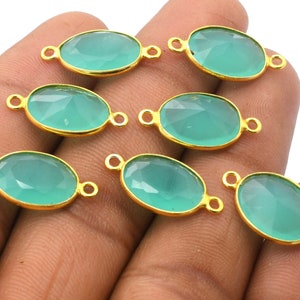 May include: Seven oval-shaped green gemstone pendants with gold-toned jump rings. The gemstones are faceted and have a translucent appearance.