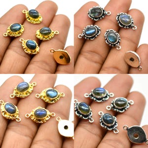 May include: A set of eight silver and gold tone connector charms featuring oval-shaped labradorite gemstones. The charms have a loop on one end and two loops on the other end.