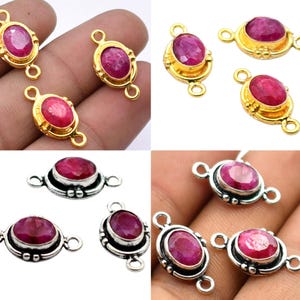 May include: Jewelry components featuring oval-cut, deep red gemstones. The components are set in gold and silver metal settings. The gold settings have a decorative border, while the silver settings have a more minimalist design. Each component has loops for attachment.