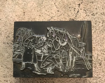 May include: A rectangular, black printing block with a detailed relief carving depicting a horse-drawn carriage scene. The image shows a horse, people, and a tree. The block is likely used for printmaking or letterpress.