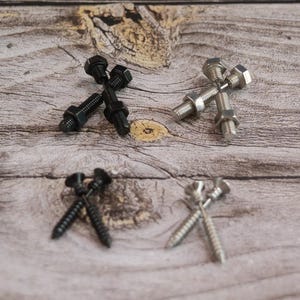 May include: A selection of hardware, including black and silver bolts, nuts, and screws, arranged on a wooden surface. The fasteners are displayed in pairs, showcasing their design and metallic finishes. The image highlights the variety of hardware.