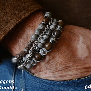 May include: Three beaded bracelets in shades of grey, brown, and silver, stacked on a wrist. The bracelets feature various bead sizes and a silver chain. Text reads "Dragons & Knights".