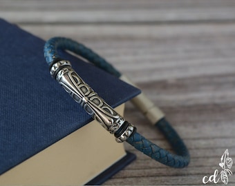 May include: A blue leather bracelet with a silver metal clasp featuring an intricate design. The bracelet is woven and has a textured look.