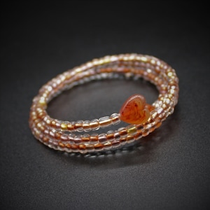 May include: A multi-strand beaded bracelet with a heart-shaped carnelian charm. The bracelet is made with clear, gold, and pink beads.