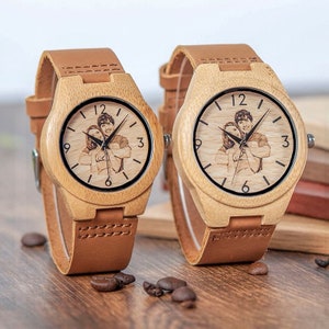 May include: Two wooden wristwatches with brown leather bands. The watch faces feature a photo of a couple and black hour and minute hands.