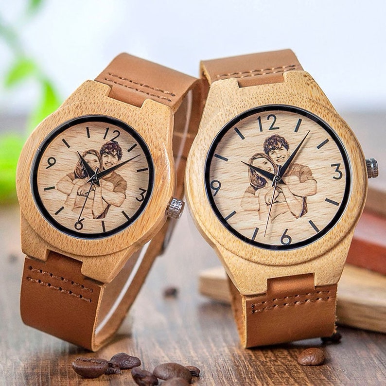 May include: Two wooden wristwatches with brown leather bands. Each watch face features a black and white photo of a couple. The watch faces have black Roman numeral hour markers.