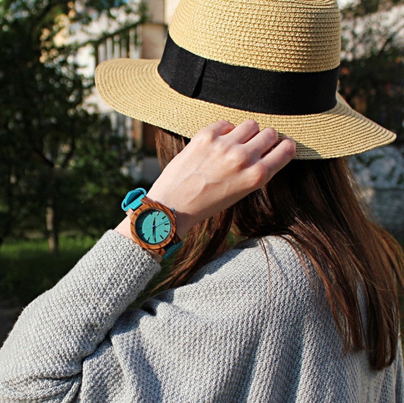 Puede incluir: Una mujer con un su&eacute;ter azul claro y un sombrero de paja con una banda negra. Lleva un reloj de madera con una esfera turquesa y una banda azul.