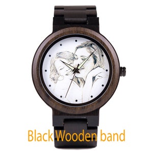 May include: A black wooden wristwatch with a white face featuring a black and white photo of a mother and child. The watch has a black wooden band.