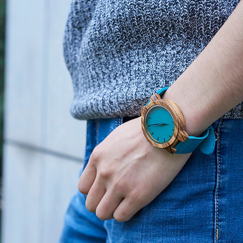 Puede incluir: Un reloj de pulsera de madera con una esfera azul turquesa y una correa de cuero azul turquesa.
