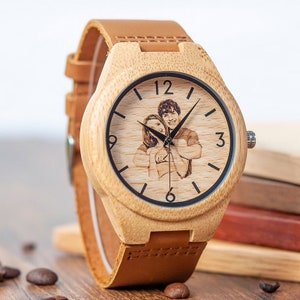 May include: A light brown wooden wristwatch with a brown leather band. The watch face has a black border and a photo of a couple is engraved in the center. The numbers 12, 3, and 6 are visible on the watch face.