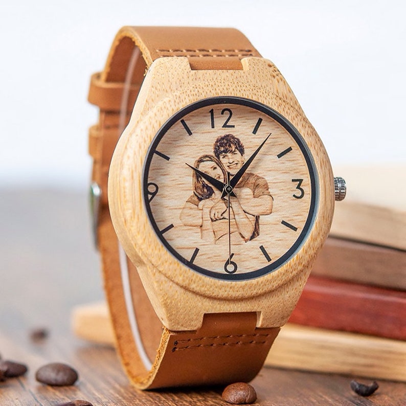 May include: A light brown wooden wristwatch with a brown leather band. The watch face has a black border and a photo of a couple is engraved in the center. The numbers 12, 3, and 6 are visible on the watch face.