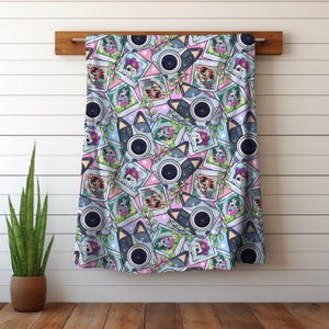 May include: A pink and blue patterned fabric with a repeating design of cameras and leaves. The cameras are decorated with cartoon dog faces and have a white border. The leaves are green and have a white outline.