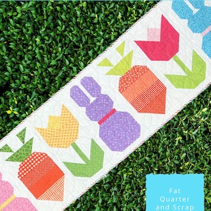 Könnte beinhalten: Ein weißer Tischläufer mit einem farbenfrohen Design aus einem Hasen, Tulpen und Karotten. Der Tischläufer ist 56 cm breit und 178 cm lang und wurde aus Fat Quarters und Resten gefertigt. Der Text "The Tipsy Needle" befindet sich in der oberen linken Ecke des Bildes.