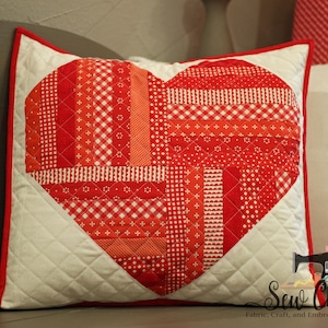 May include: A red and white heart-shaped pillow with a patchwork design. The pillow is made of various red and white fabrics, including gingham and stripes. The pillow is surrounded by a white fabric with a red border.