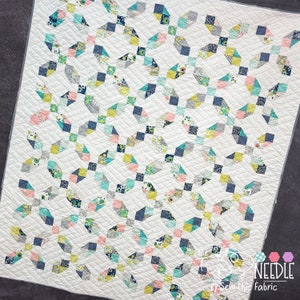 May include: A white quilt with a geometric pattern in shades of blue, green, yellow, and pink. The quilt is made up of small squares and is quilted with a diamond pattern. The quilt is labeled "The Pretty Needle by Sew Chic Fabric."