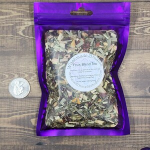 May include: A purple resealable pouch filled with a fruit blend tea. The pouch has a white label with the text "Witchmade Studios Fruit Blend Tea" and instructions for brewing the tea. The label also includes the website address "www.witchmadestudios.com".
