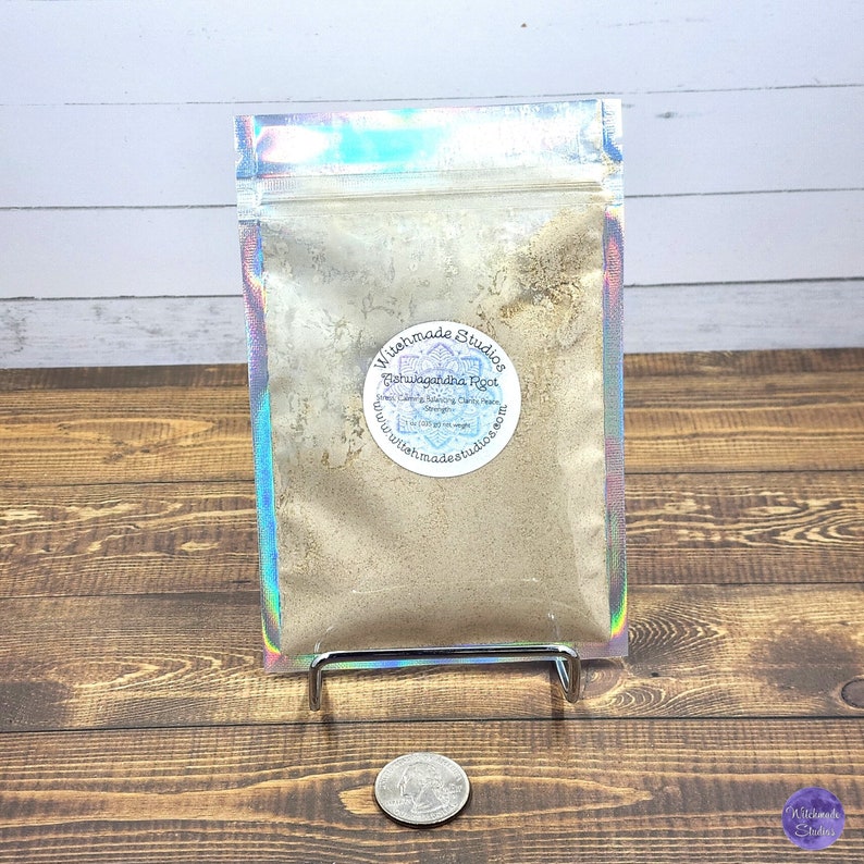 May include: A silver iridescent resealable pouch containing a light brown powder. The pouch has a white label with the text "Witchmade Studios Ashwagandha Root" and a website address.