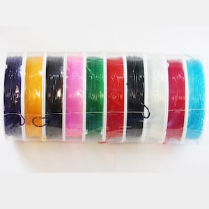 May include: A set of ten spools of elastic cord in various colors, including purple, yellow, black, pink, green, red, clear, white, red, and blue. The spools are wrapped in clear plastic and have a white label.
