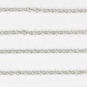 May include: Close-up of several silver-coloured chain necklaces. The chains are made of small, oval-shaped links. The chains are displayed against a white background.