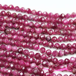May include: A strand of pink ruby beads, faceted and polished, with a slightly rough texture. The beads are strung on a thin pink thread.