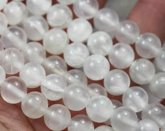 May include: A strand of white moonstone beads, each bead is round and smooth. The beads are strung together on a clear thread.