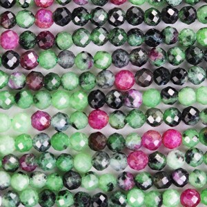 May include: Close-up of a collection of faceted gemstone beads. The beads are a mix of green, black, and pink hues, strung together in parallel rows. The beads have a polished, reflective surface, and are likely used for jewelry making.