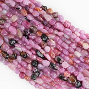 May include: A strand of pink and black gemstone beads. The beads are irregularly shaped and have a smooth, polished finish.