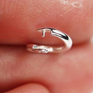 May include: A small, polished silver hoop earring featuring a hinged mechanism with a thin post that inserts into the opposite end of the circular band. The metal surface is smooth and reflective, showing a bright metallic finish throughout.