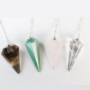 May include: Four crystal pendulums with silver chains. The pendulums are in the shapes of pointed cones. The crystals are clear, green, brown, and pink.
